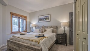 Quarto com cama de madeira, duas mesas de cabeceira, uma janela com vista e uma porta.