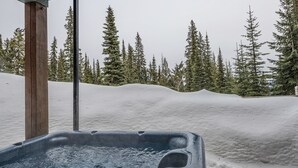 Uma banheira de hidromassagem em ambiente externo coberto de neve, com um poste de madeira e chão com neve.