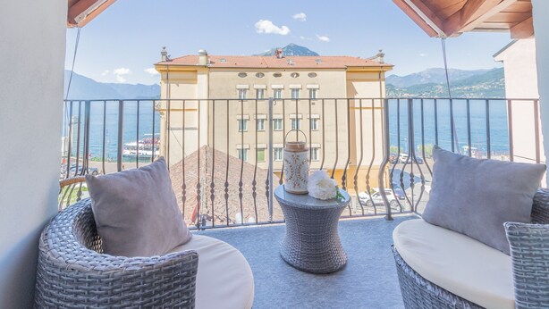 Un balcon agrémenté de meubles en osier, d’un vase décoratif et offrant une vue sur une montagne et la mer.
