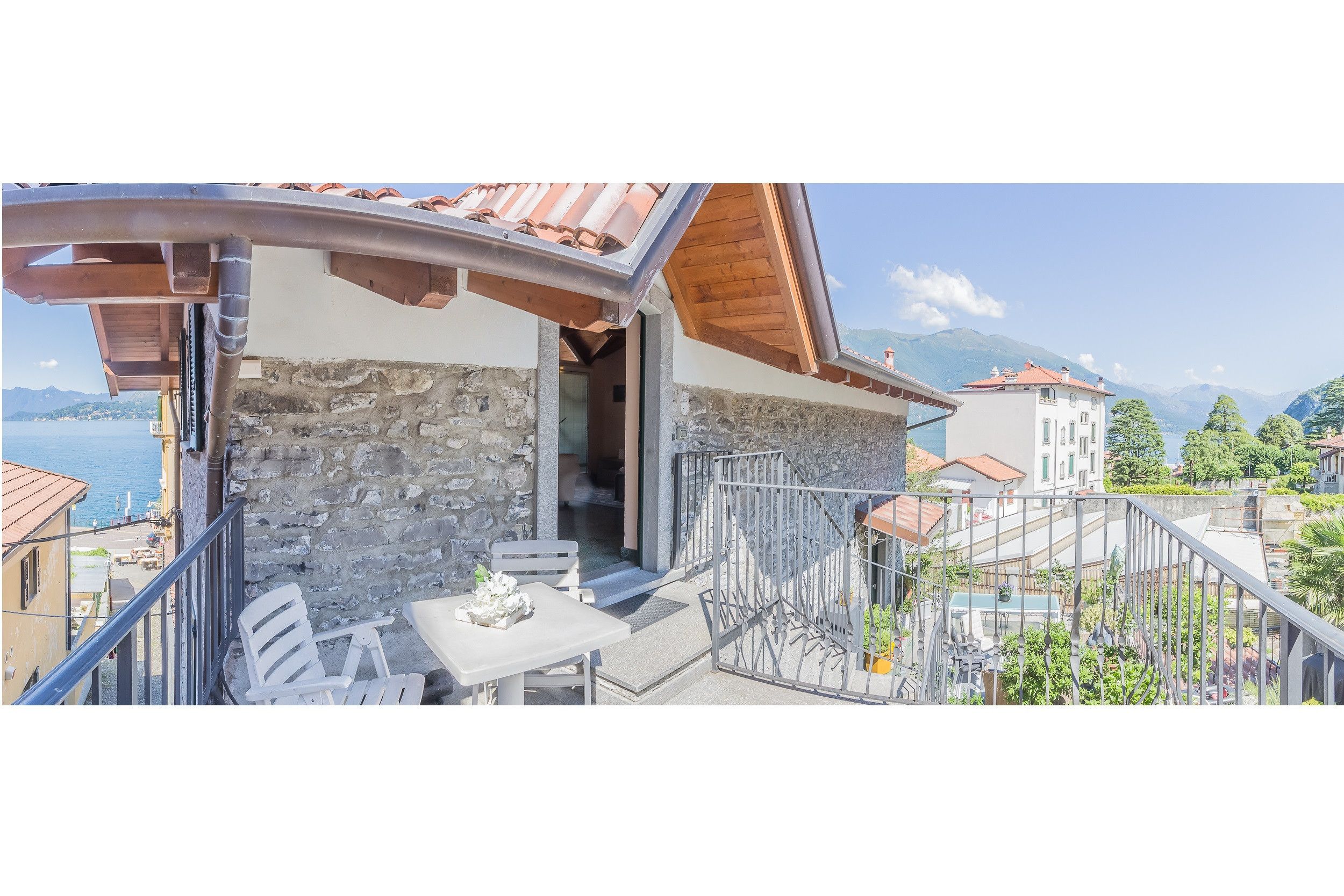 Un balcone con parete in pietra, soffitto in legno e vista su un lago e montagne.