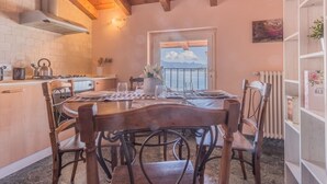 Une cuisine chaleureuse avec des poutres en bois, une table à manger avec des chaises, une vue sur la mer par la fenêtre et une bibliothèque agrémentée d’une décoration florale.