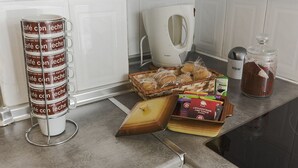 A kitchen counter with a coffee maker, a jar of sugar, a basket of pastries, a stack of coffee mugs, and a box of tea bags. - 4 Bed-Sleeps 6-Garden-Balcony-Pets (Alcalá de Henares)