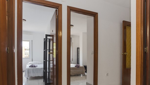 A hallway with wooden doors leading to a bedroom with a bed and a wardrobe. - 4 Bed-Sleeps 6-Garden-Balcony-Pets (Alcalá de Henares)