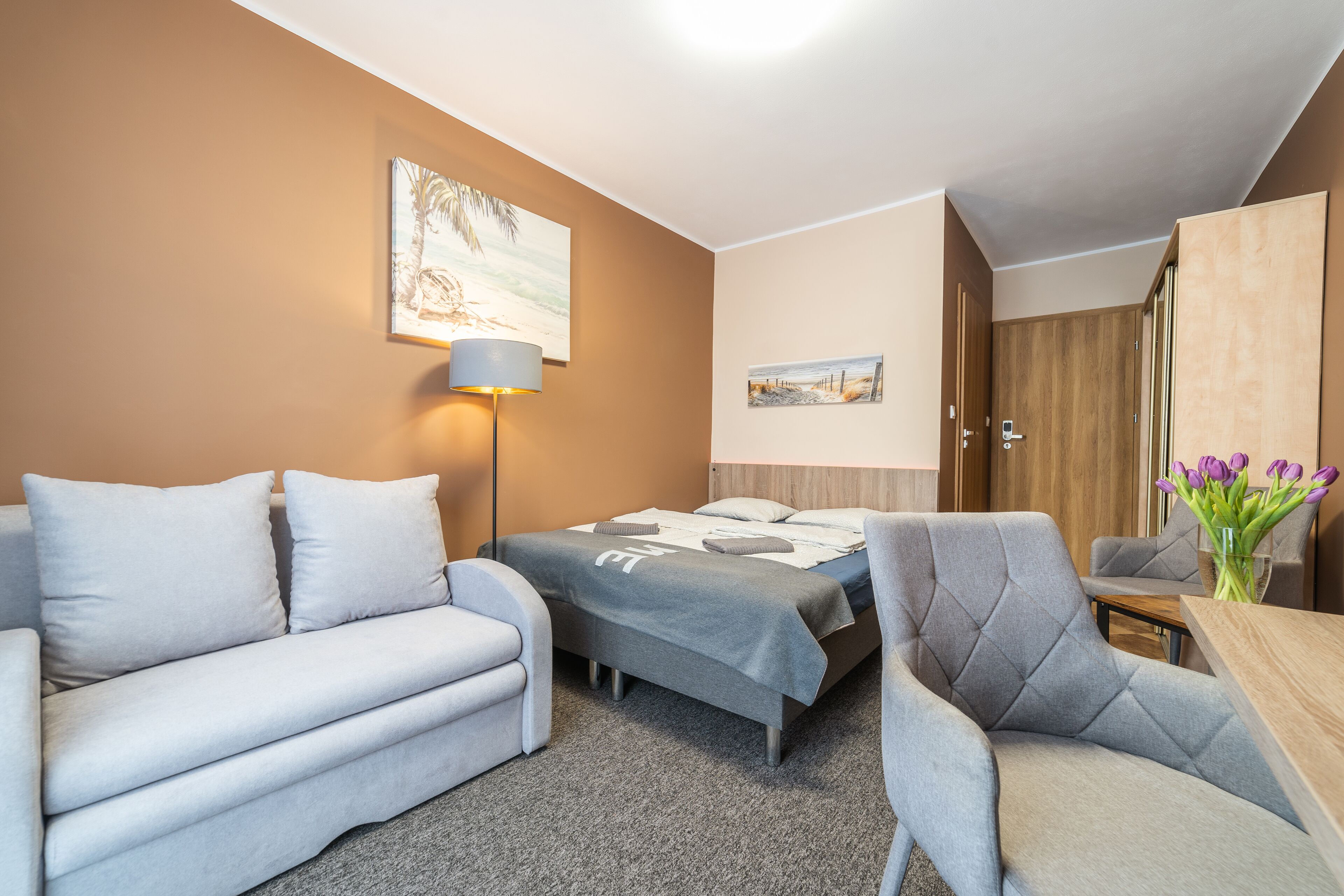 Une chambre d’hôtel avec un lit, un canapé, une chaise, une lampe et un tableau au mur.
