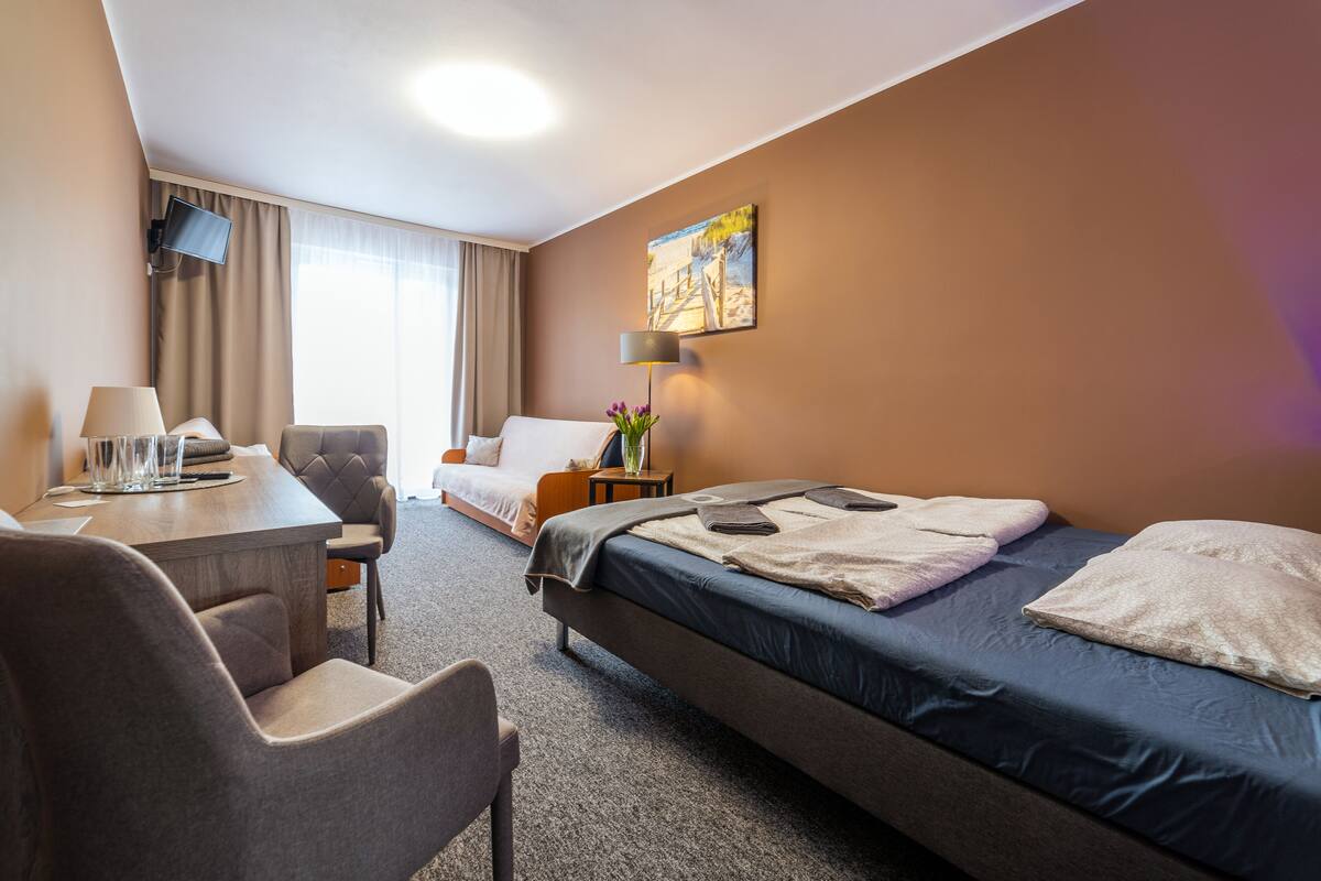 A hotel room with a bed, a desk, a chair, a TV, and a painting on the wall.