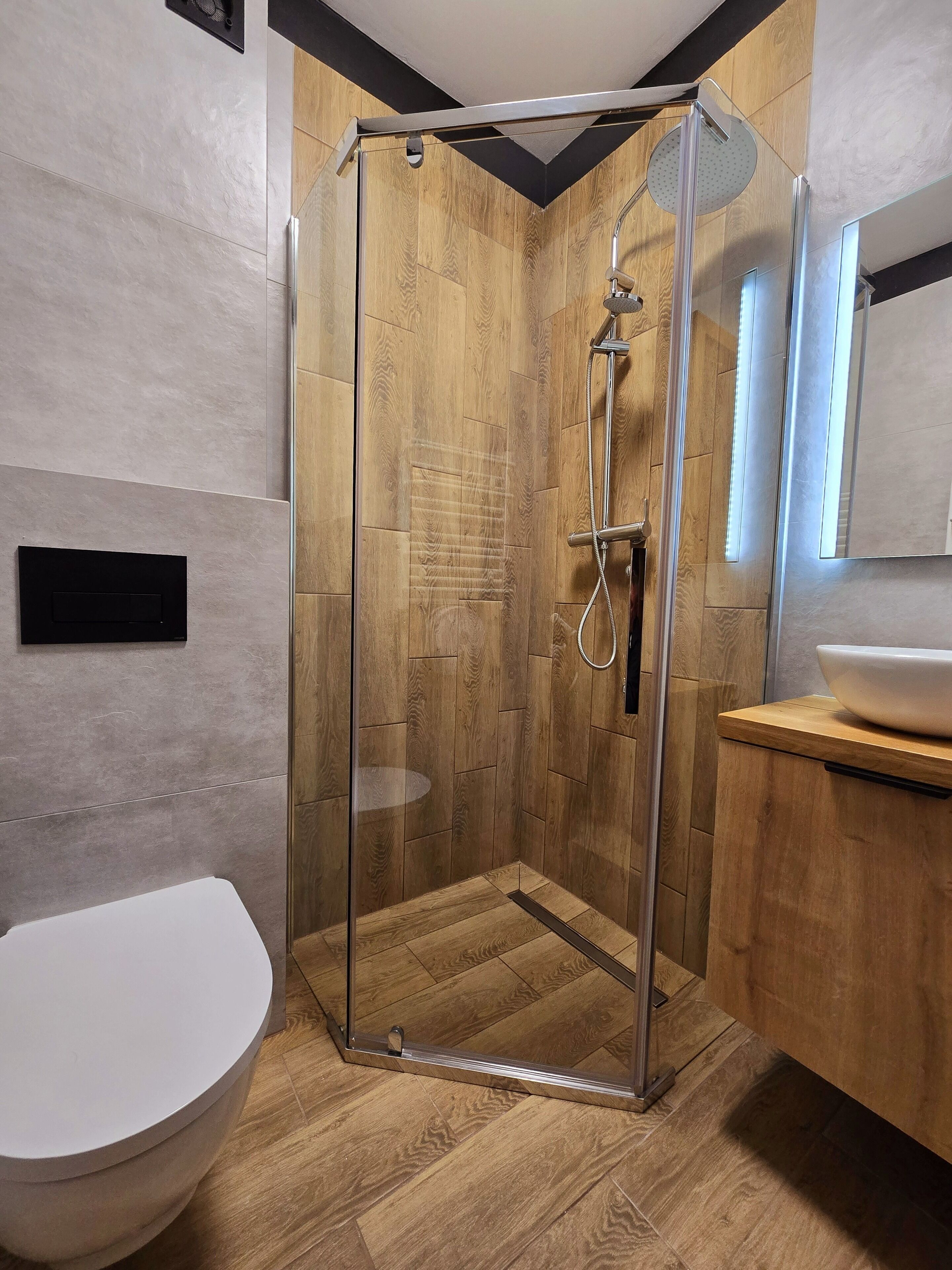 A modern bathroom with a glass-enclosed shower, a white toilet, and a wooden vanity with a mirror.