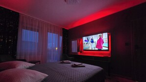 Una camera d'albergo scarsamente illuminata, con un letto grande, una televisione a parete e una finestra con tende.
