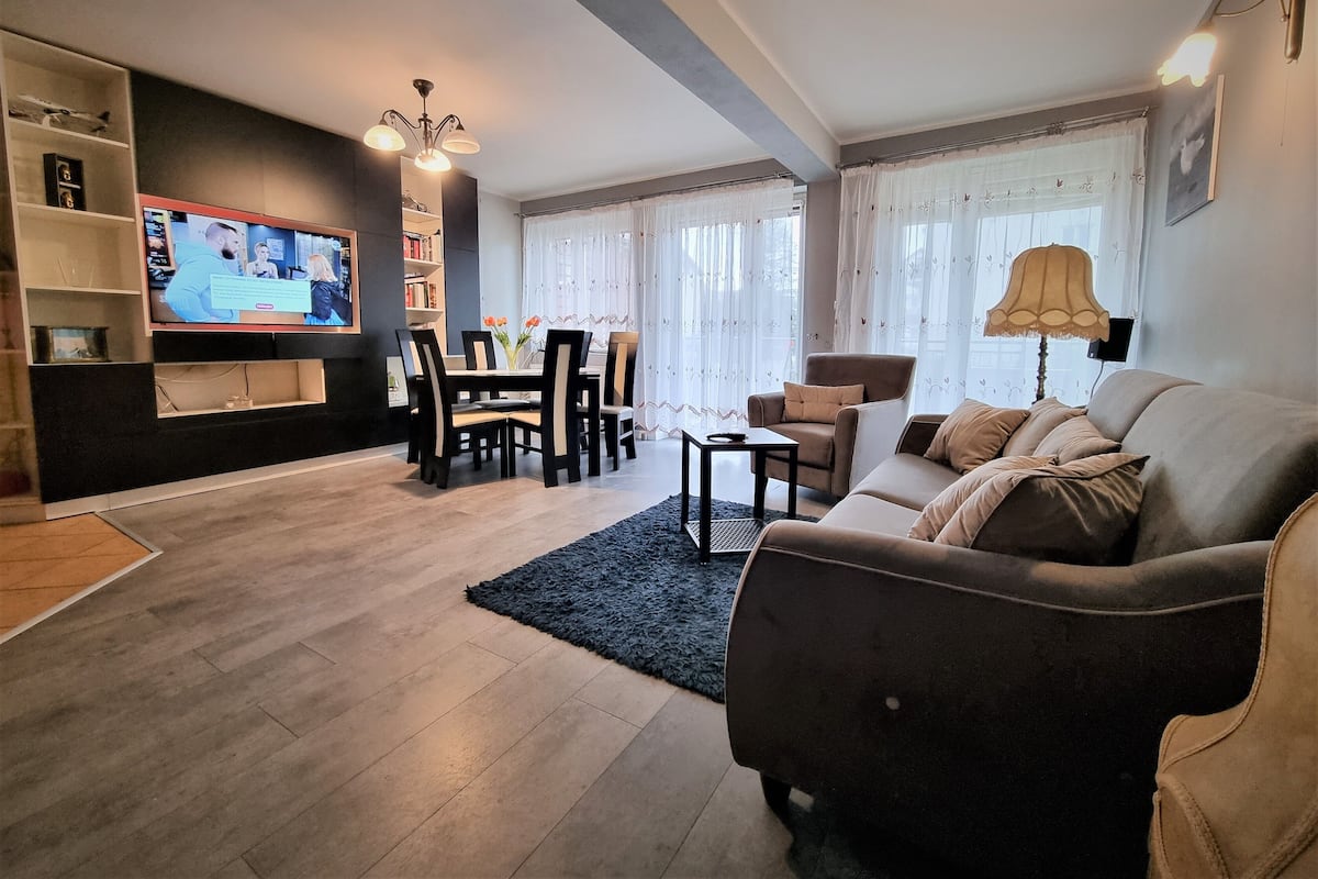 A living room with a sofa, TV, dining table, chairs, and a bookshelf.