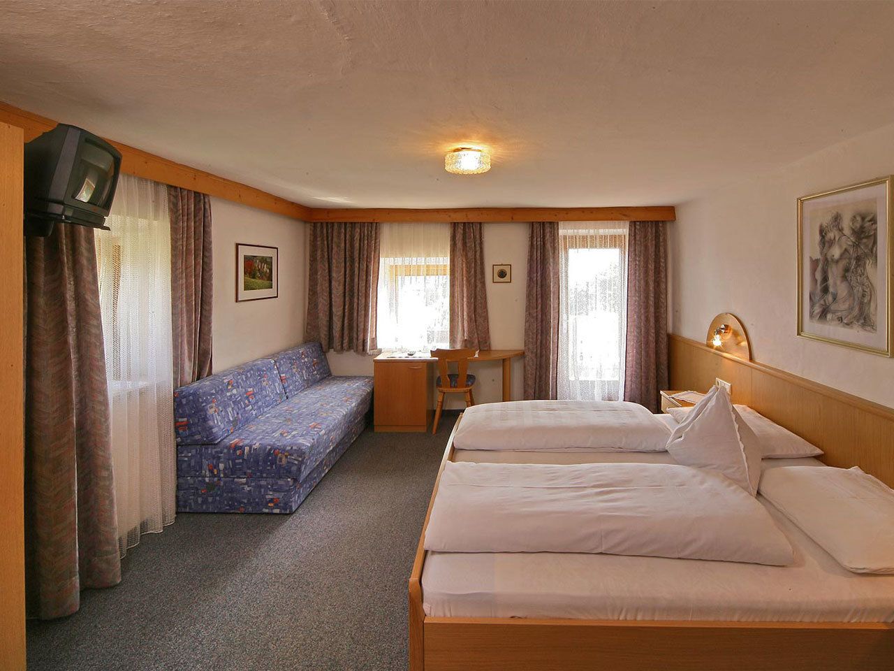 A hotel room with two beds, a sofa, a desk, and a television.