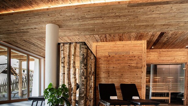 Un intérieur en bois avec un banc et des chaises, une grande colonne et une vue à travers une porte vitrée.