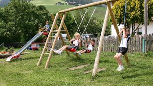 Un terrain de jeux avec des balançoires et un toboggan, situé dans un espace verdoyant avec une montagne en toile de fond.
