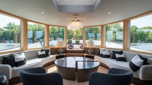 Un salon moderne avec une table ronde en verre, des sièges confortables et de grandes fenêtres donnant sur l’eau.