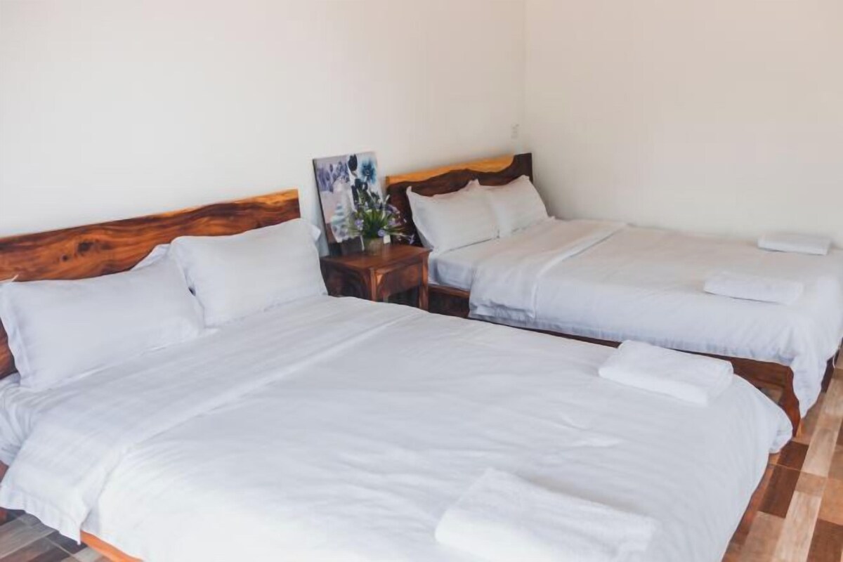 Ein Hotelzimmer mit zwei Einzelbetten, Holz-Kopfteilen, weißen Bettwäsche und einem kleinen Nachttisch mit Blumen.