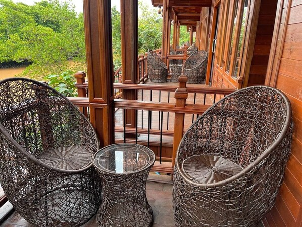 A wooden balcony with wicker chairs and a glass table.