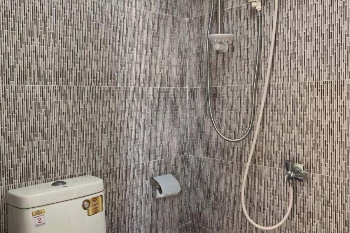 Ein Duschbereich mit strukturierter Wand, einer Handbrause und einem WC mit sichtbarer Beschriftung.