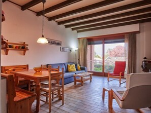 Un accogliente soggiorno con tavolo da pranzo in legno, divano blu e una poltrona rossa. Presente un balcone con vista su alberi e un edificio.