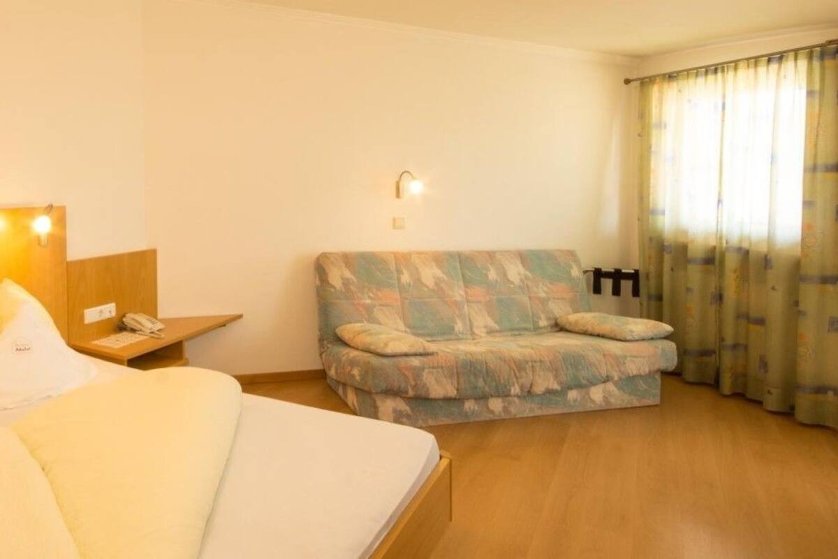 Una habitación de hotel con cama, sofá, mesita de noche y lámpara.