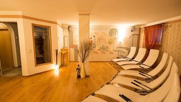 A room with a wooden floor, a reception desk, a mural, and several reclining chairs.