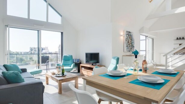 A modern living room with a dining area, large windows, and a staircase. - Parc Océan by Interhome (Quiberon)