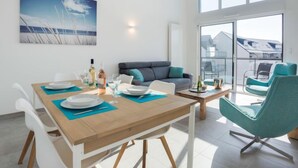 A modern living room with a dining area, featuring a large window, a sofa, and a table set for dining. - Parc Océan by Interhome (Quiberon)