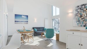 A modern living room with a dining area, a sofa, a teal chair, and a kitchen area with cabinets. - Parc Océan by Interhome (Quiberon)