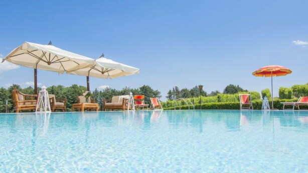 Ein klares Schwimmbecken mit Liegestühlen und Sonnenschirmen, umgeben von viel Grün.