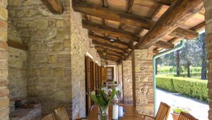 Ein patio mit Steinmauern, bedeckt, mit einem Holztisch und Stühlen, einer Vase mit Blumen und Blick auf einen angelegten Garten.
