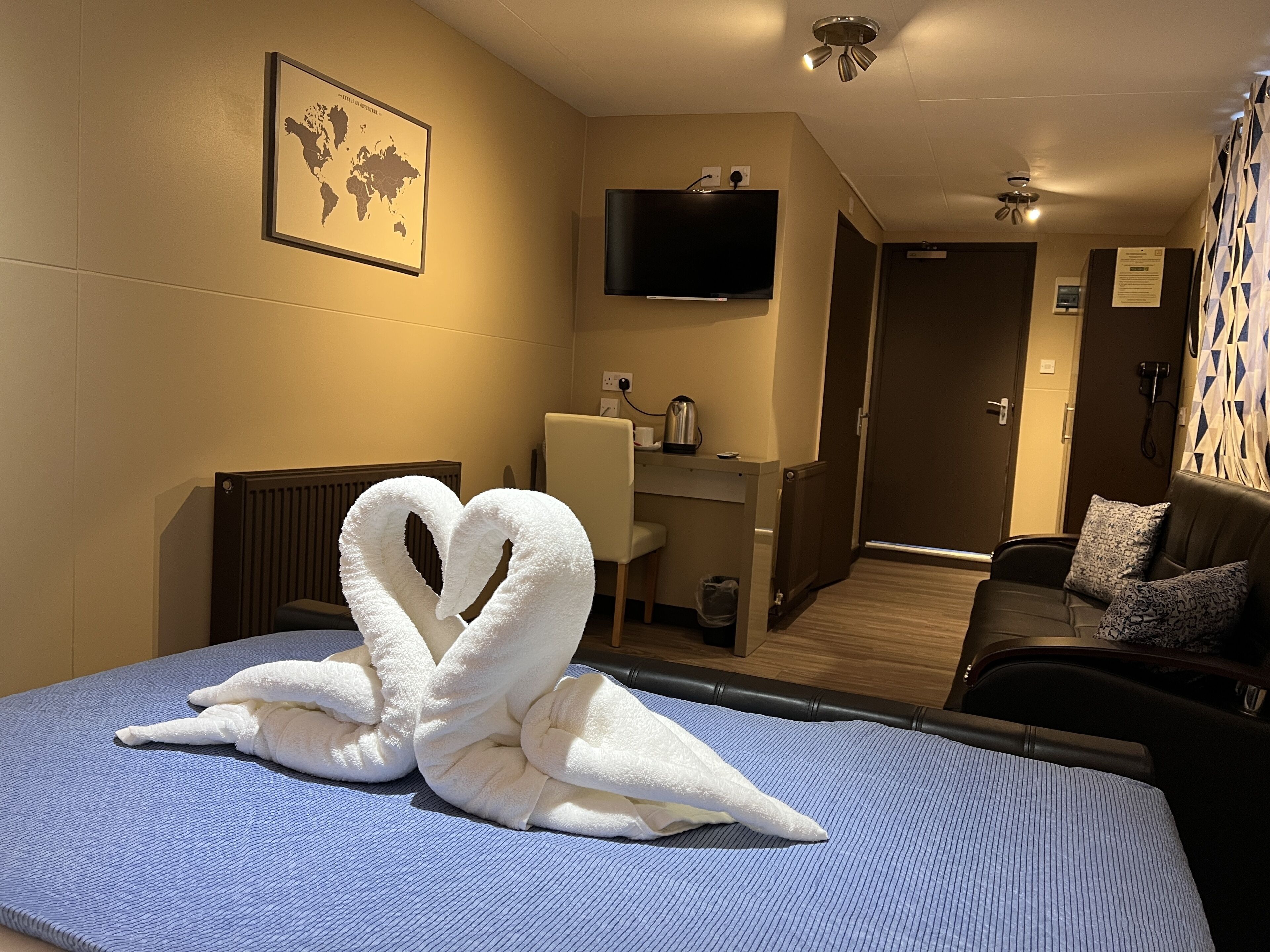 A hotel room with a bed, a desk, a chair, a TV, and a world map on the wall.