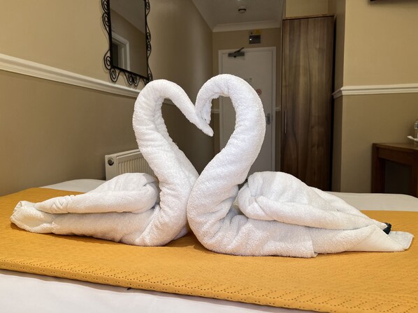A bed with a towel arranged in the shape of two swans.
