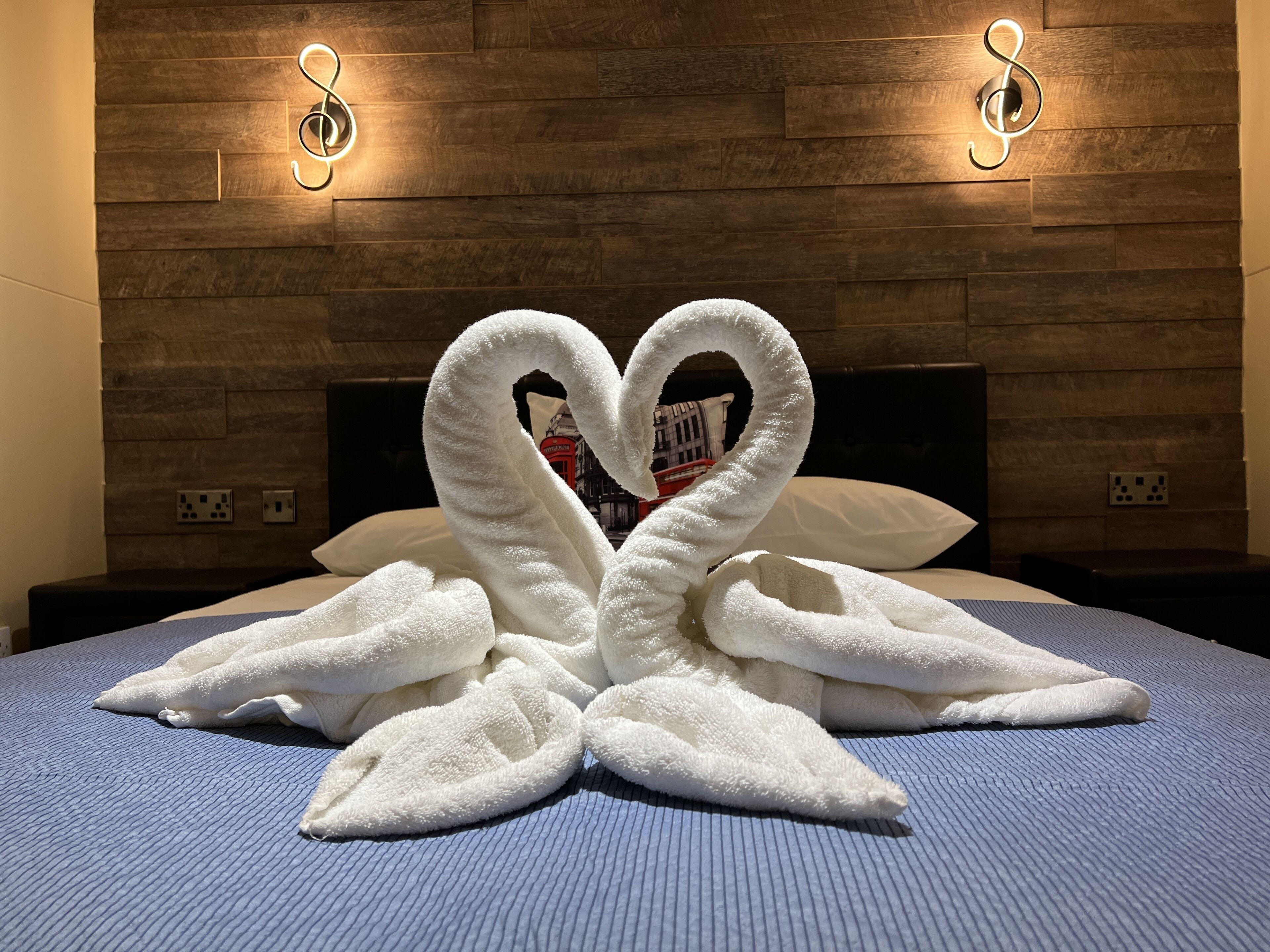 A bed with a blue textured cover and a heart-shaped towel arrangement on it.