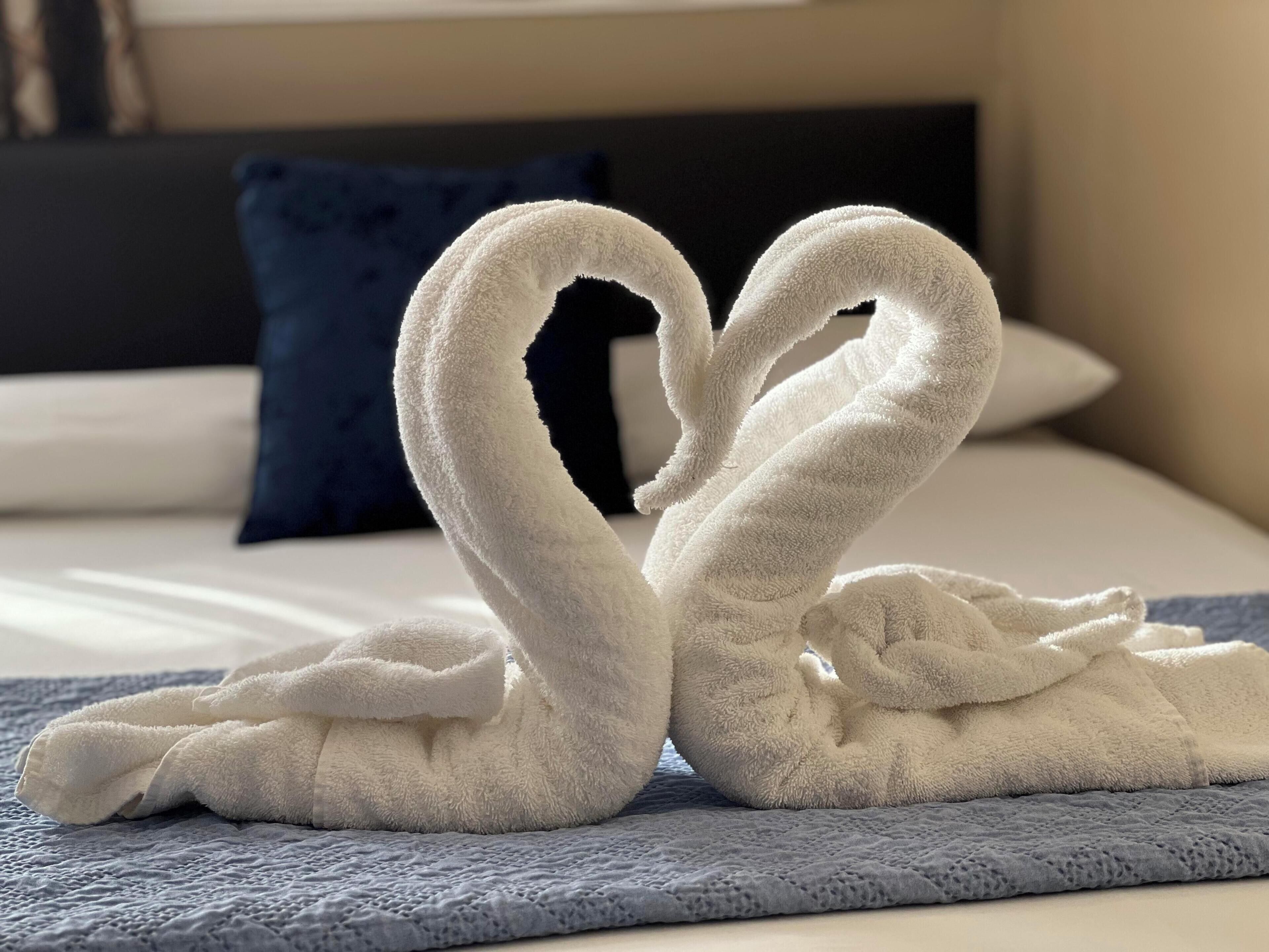 A bed with a blue blanket and a heart-shaped towel arrangement.