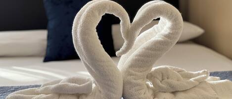A bed with a blue blanket and a heart-shaped towel arrangement.