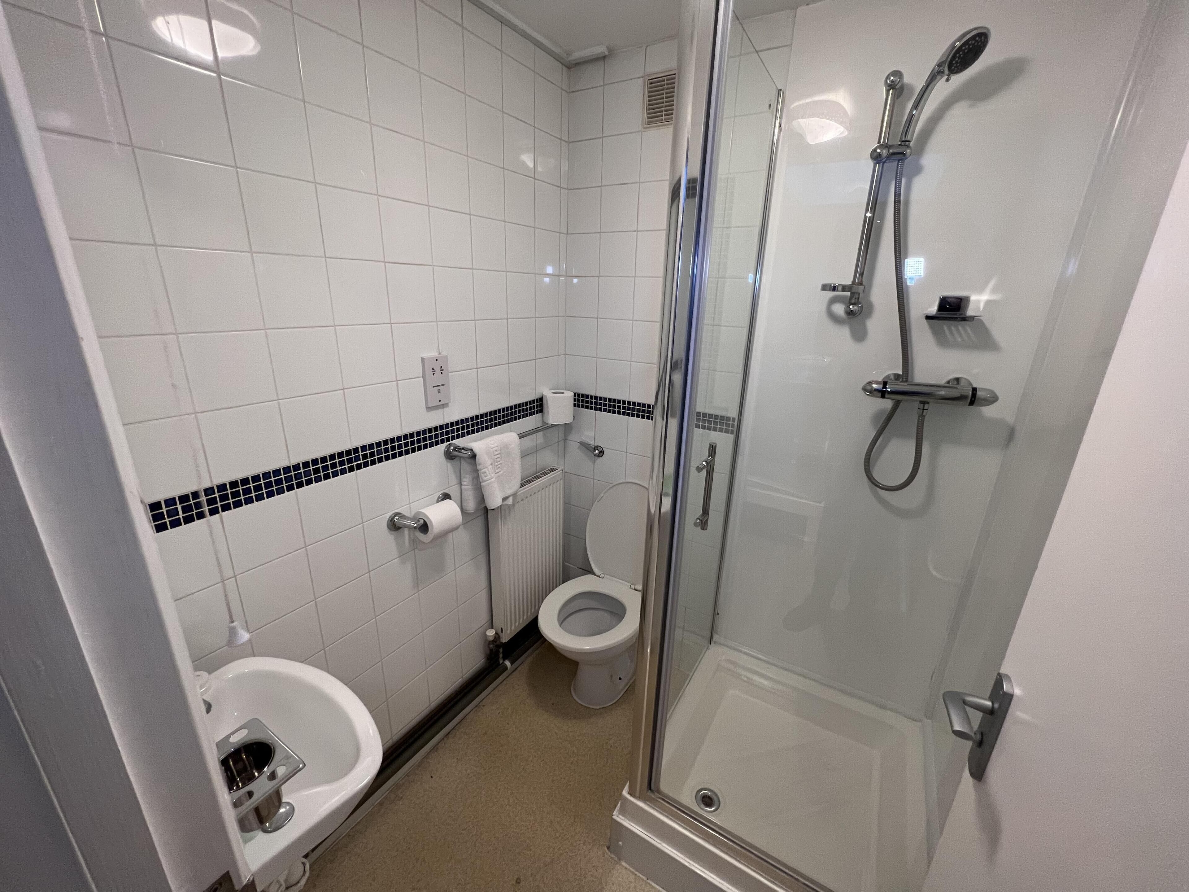 Um banheiro com chuveiro em cabine de vidro, vaso sanitário e pia.