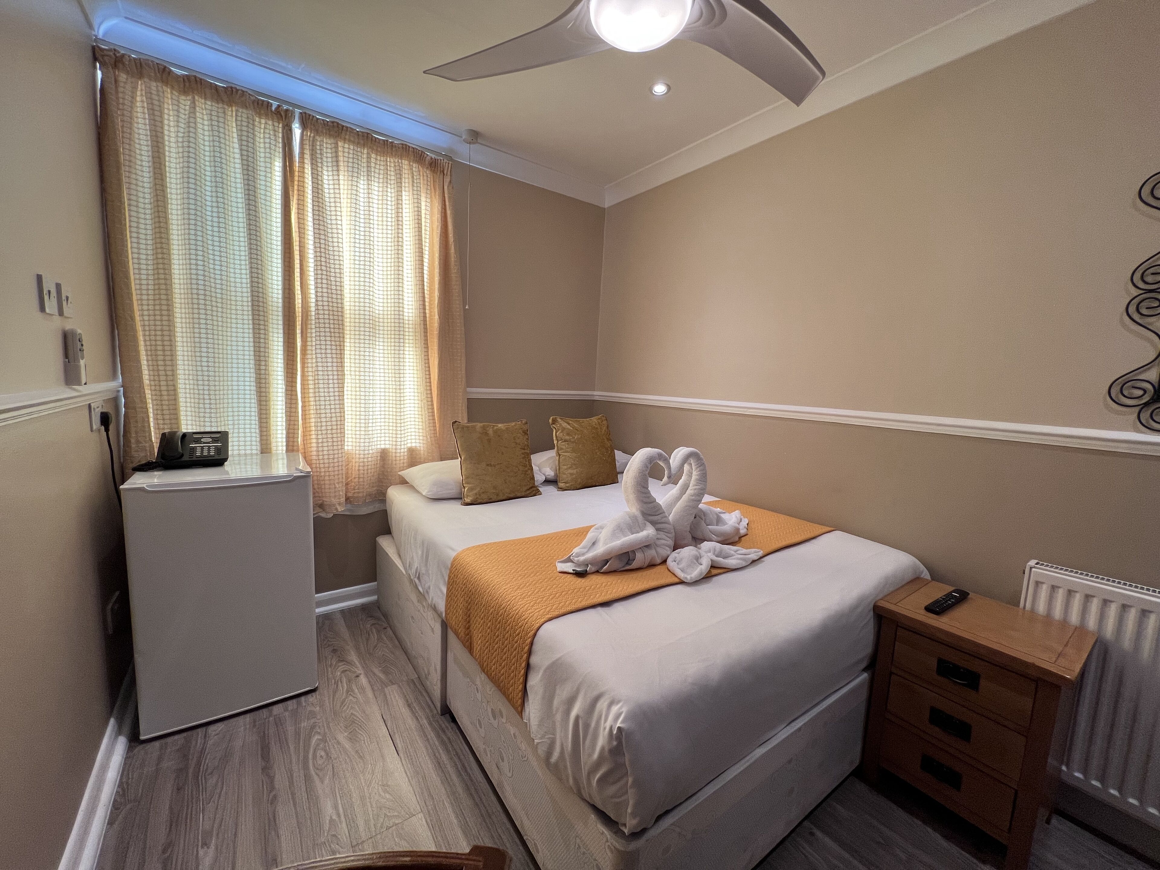 Une chambre d’hôtel avec un lit, une table de chevet, un radiateur et un téléphone posé sur un bureau.