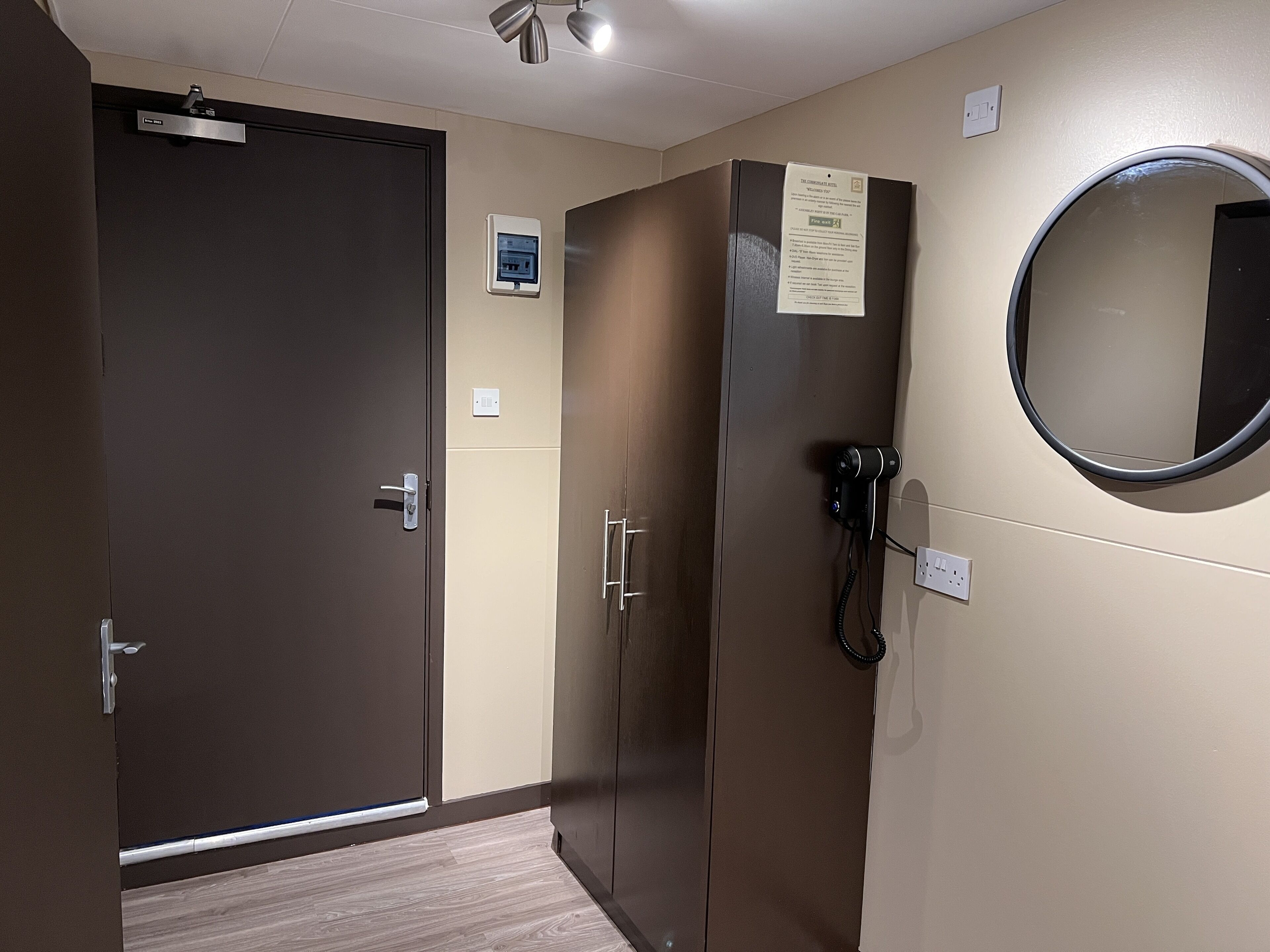 Habitación de hotel con puerta cerrada, armario, teléfono, enchufe y espejo.