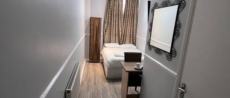 A narrow hallway with a bed, a desk, and a radiator.
