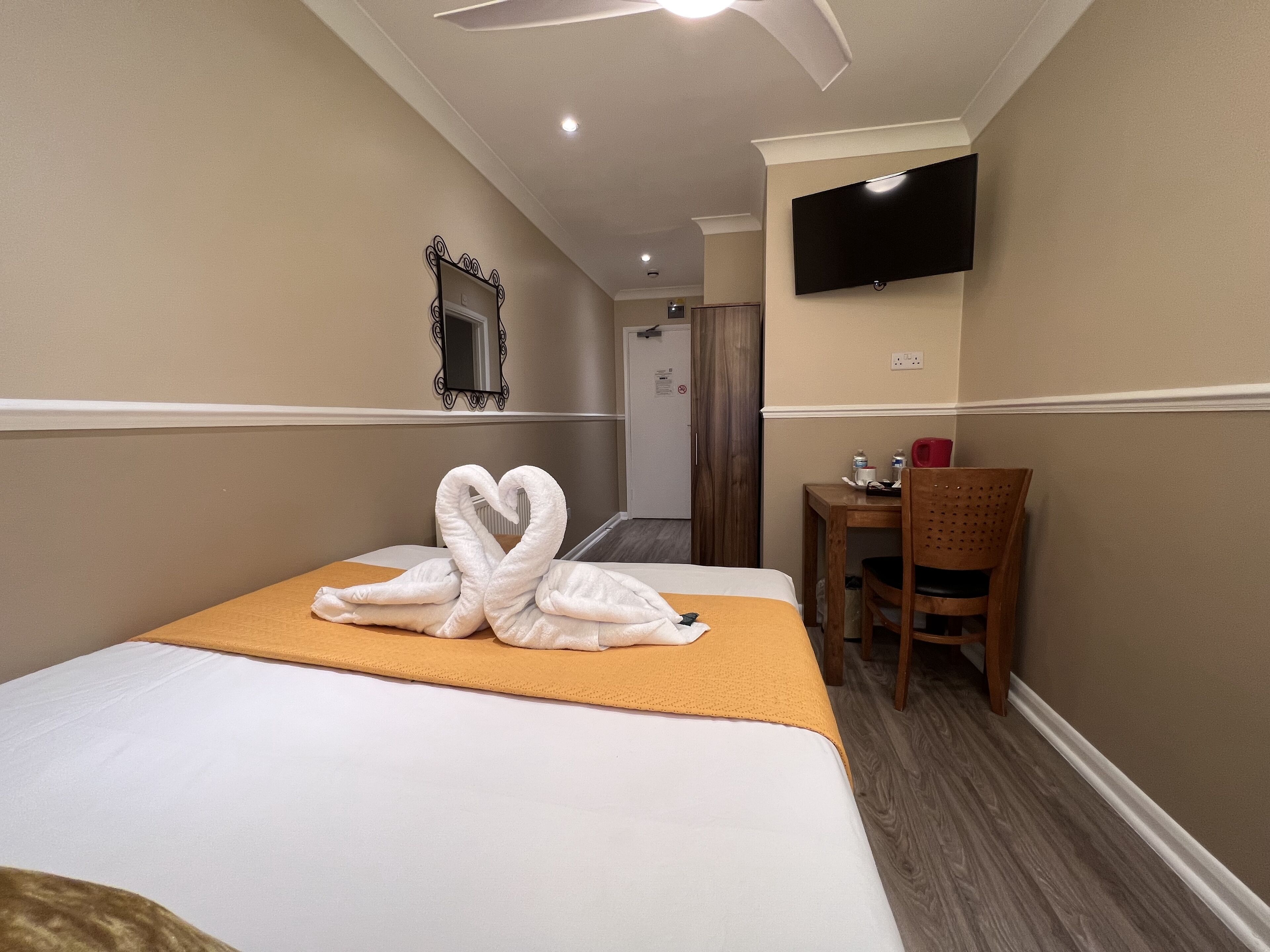 A hotel room with a bed, a desk, a chair, a flat-screen TV mounted on the wall, and a mirror on the wall.