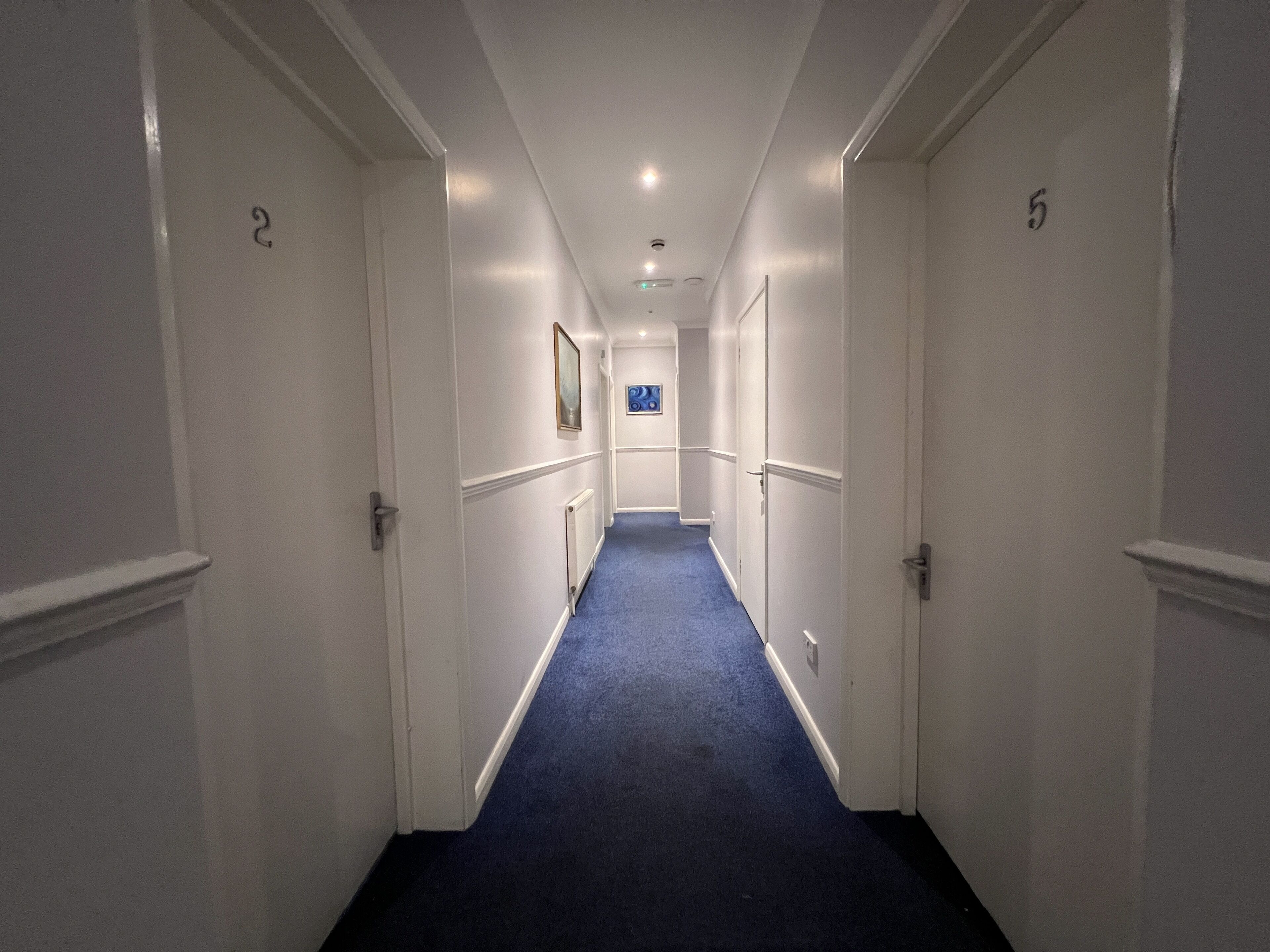 A narrow hallway with white walls and blue carpet, featuring doors numbered 2 and 5.
