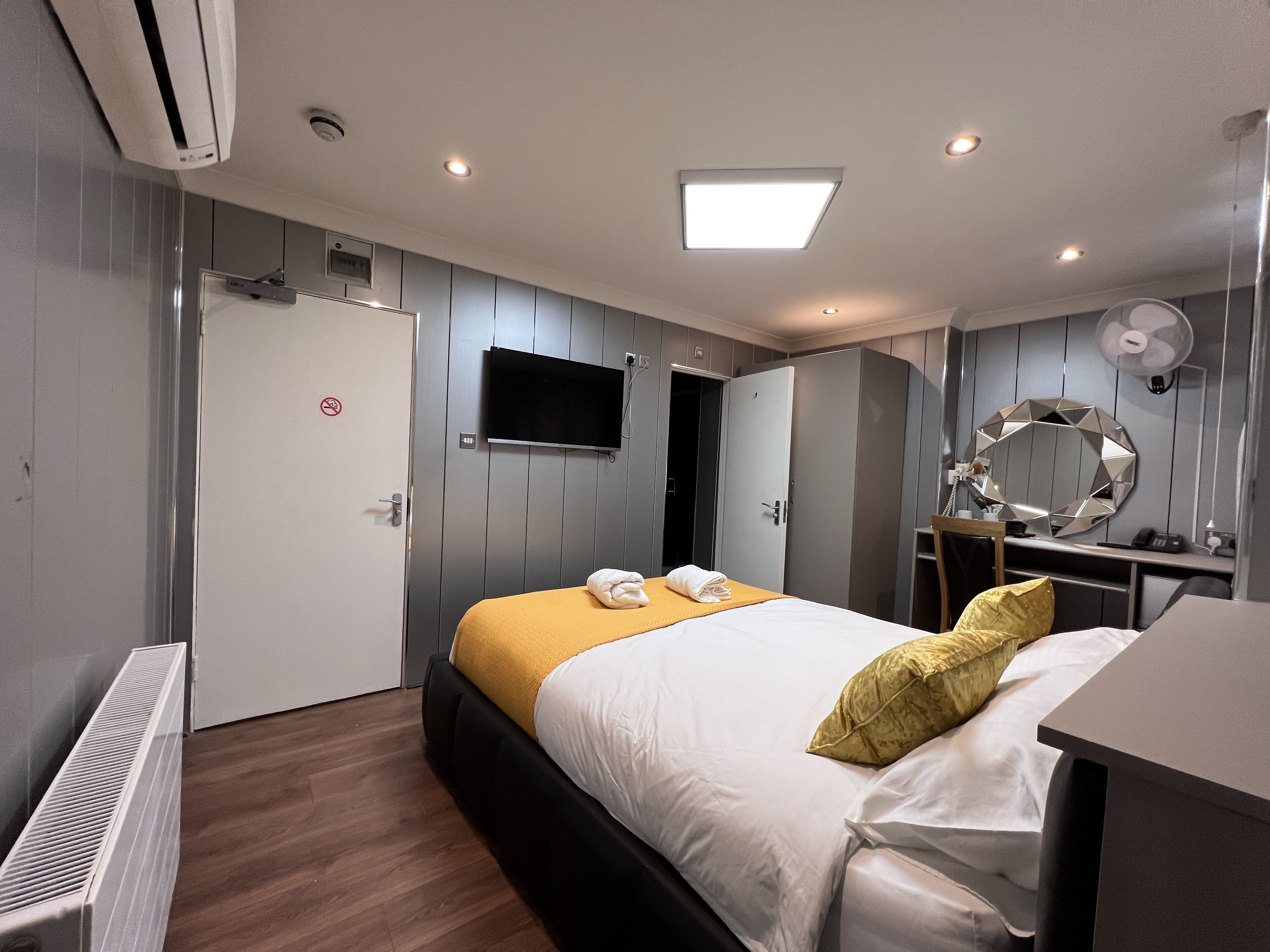 A modern hotel room with a bed, a desk, a mirror, and a TV.