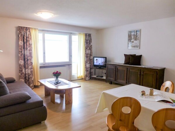 A living room with a sofa, a dining table with chairs, a television, and a cabinet.