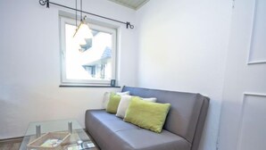 A modern living room with a grey sofa, green and white cushions, a glass coffee table, and a window with a view of buildings. - Max & Moritz Top 16 by Interhome (Zell am See)
