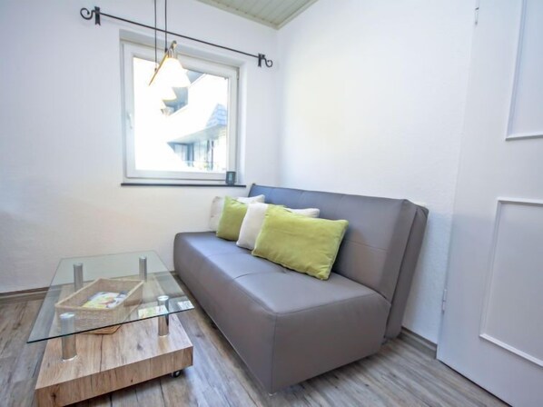 A modern living room with a grey sofa, green and white cushions, a glass coffee table, and a window with a view of buildings.