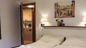 Une chambre d’hôtel avec deux lits, un tableau accroché au mur et une cuisine visible à travers une porte ouverte.