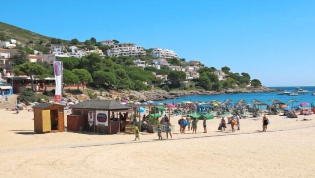 A beach with people walking, umbrellas, and a small wooden structure. - Anfora 9 by Interhome (L'Escala)
