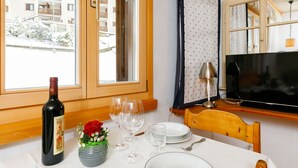 Un coin repas avec une table dressée pour deux personnes, une bouteille de vin et un vase contenant une rose rouge.