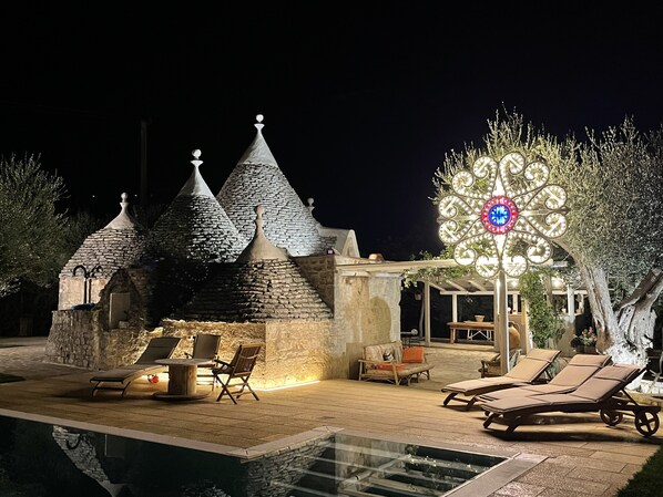 Un espace aménagé au bord de la piscine, avec des éléments en pierre, des chaises longues et un luminaire décoratif.