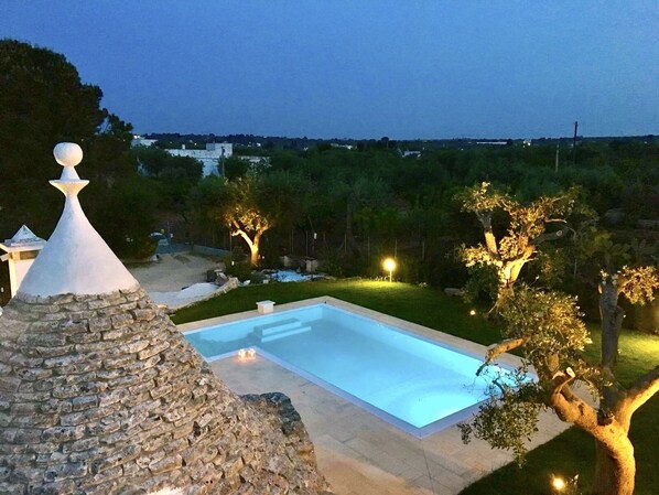 Una piscina con una estructura de piedra cerca, rodeada de árboles y vistas al paisaje.