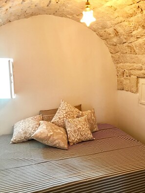 Une chambre avec un plafond en pierre, un lit avec une literie à rayures et des coussins décoratifs.