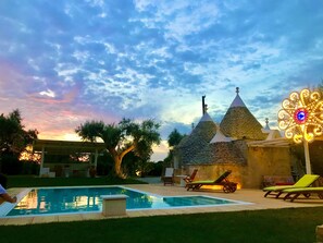 Una piscina con sillas de descanso, una luz decorativa y edificios con techo de piedra.