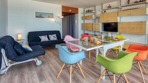 Una sala de estar moderna con sofá, sillas coloridas, una mesa de comedor y armarios empotrados de madera con un televisor.